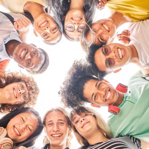 Low angle of a group of students are together, happy and smiling. Faces of young teenagers looking at camera, hugging. Vertical photo.